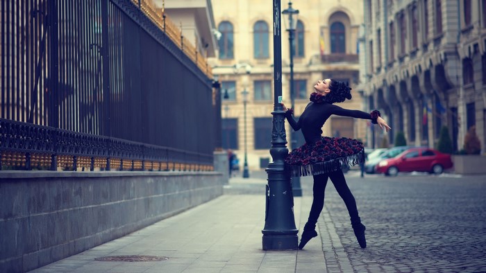 Ballerina in a black tutu dances by a lamppost on a city street