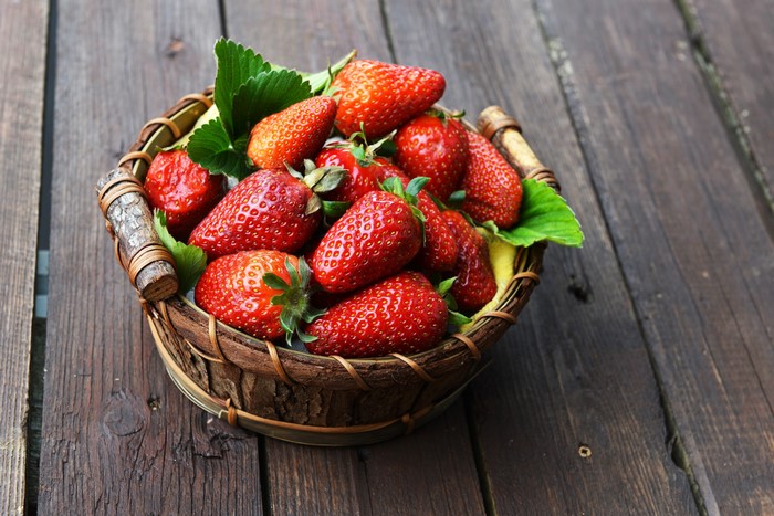 Strawberries in a wicker basket on wood planks