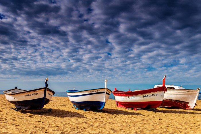Four fishing boats on a sandy beach under a cloudy sky