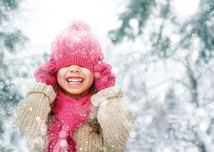 Little girl in winter hat and scarf smiling in snow