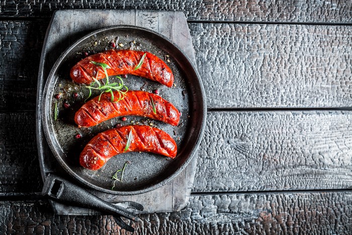 Three grilled sausages with rosemary on a pan