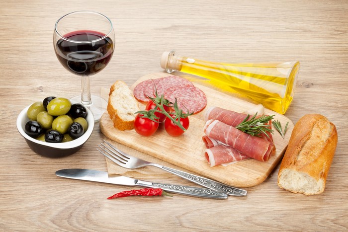 Still-life of charcuterie, olives, tomatoes, bread, and wine