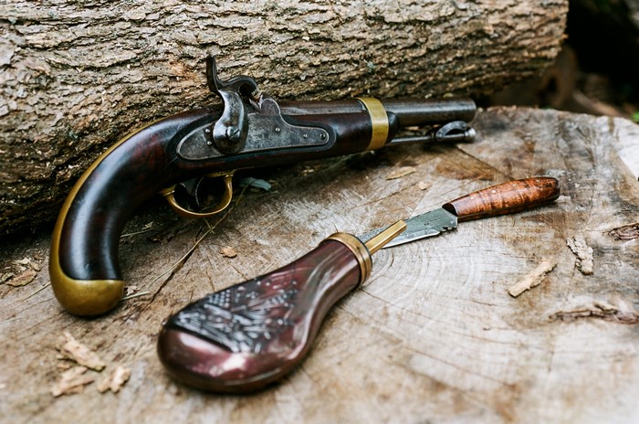 Antique pistol and knife on a log
