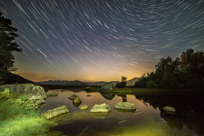 Star trails over a rocky lake at night