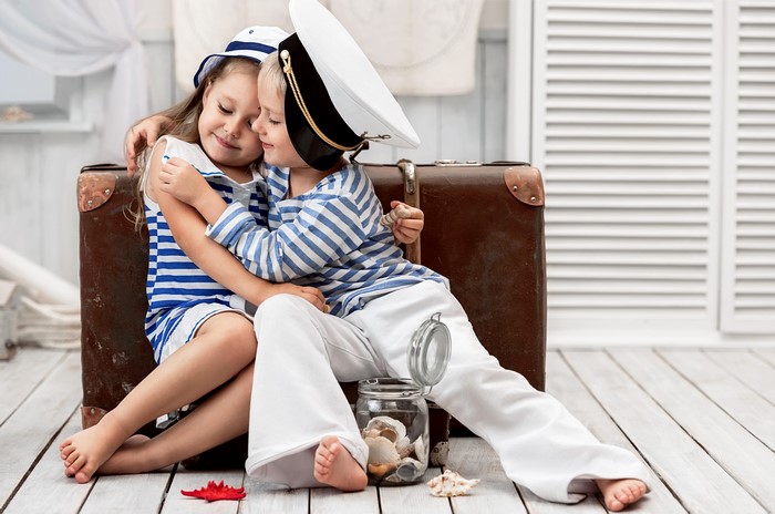 Two children in sailor outfits hugging by a suitcase