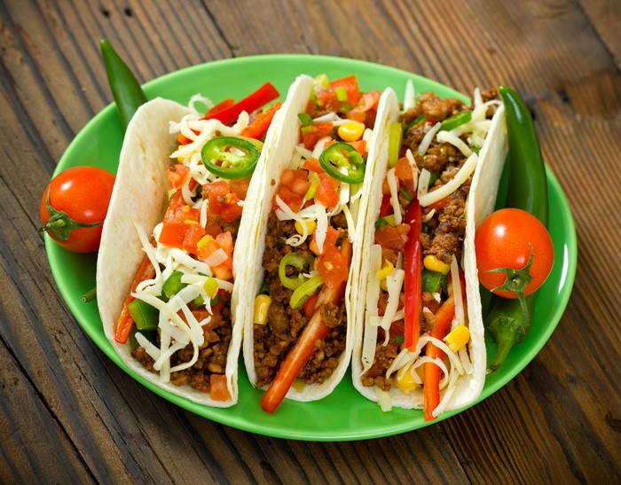Four Mexican tacos with vegetables on a green plate