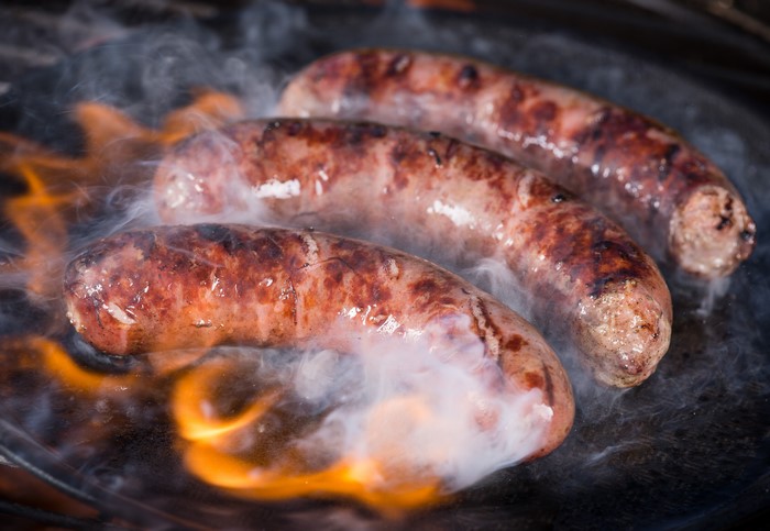Three sausages cooking on a grill with flames