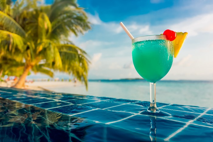 Blue cocktail with pineapple and cherry by the pool