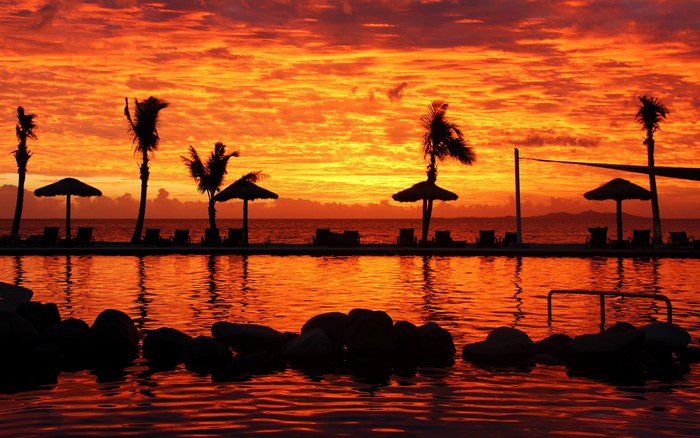 Sunset over a tropical resort pool with palm trees