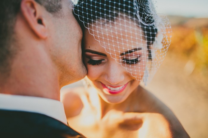 Bride wearing veil, groom kissing her cheek