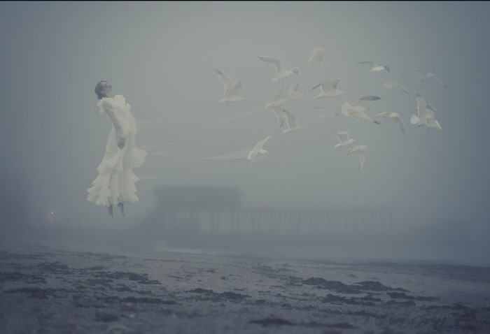 Woman in white dress floating with seagulls in fog