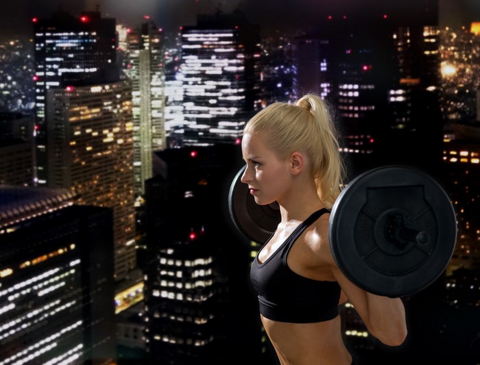 Blonde woman lifting barbell in front of city skyline at night