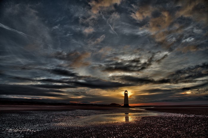 Lighthouse on a beach at sunset with dramatic clouds