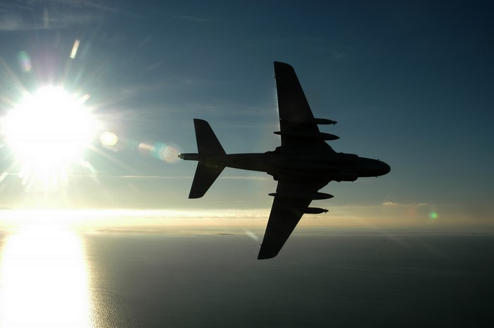Airplane silhouette against the sun over the ocean