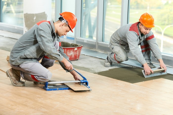 Two construction workers tiling a floor