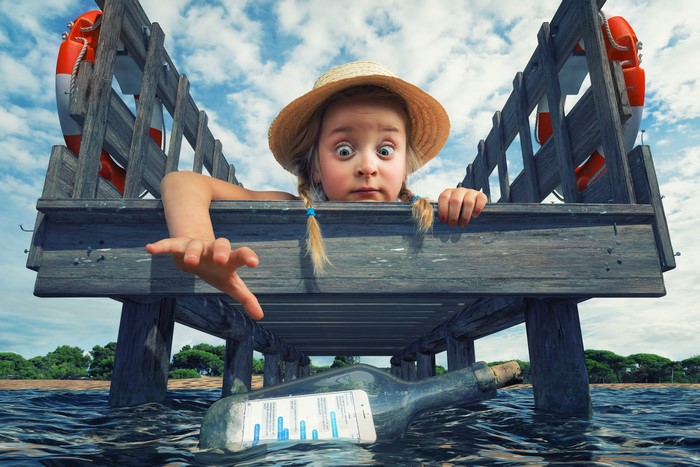 Girl reaching for a message in a bottle from a pier