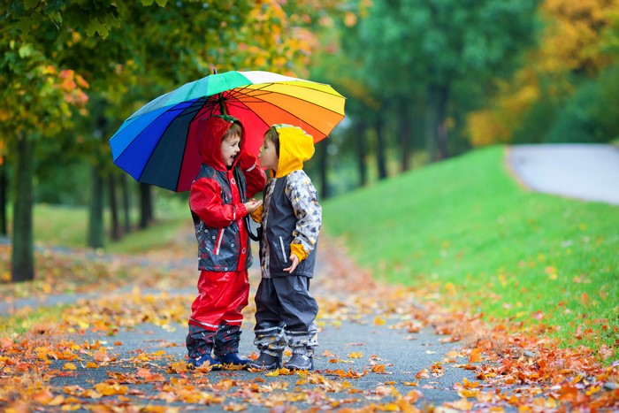 Two boys under a rainbow umbrella in autumn