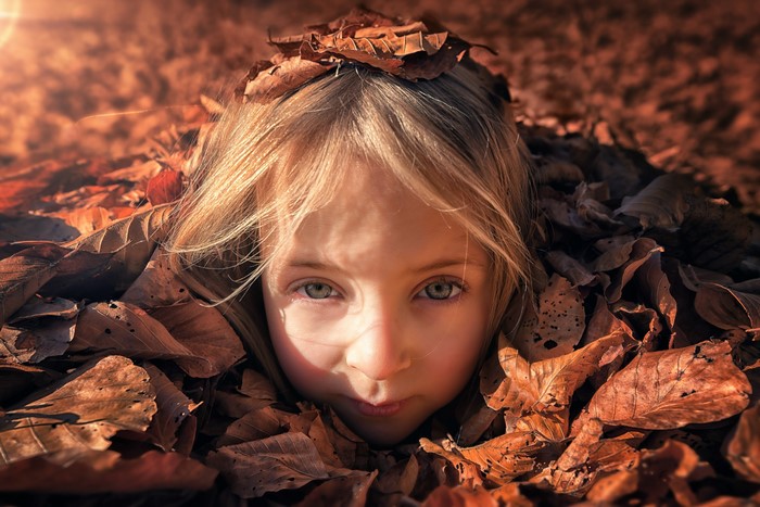 Girl peeking out from autumn leaves