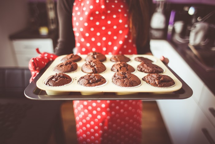 Person holding a tray of chocolate muffins
