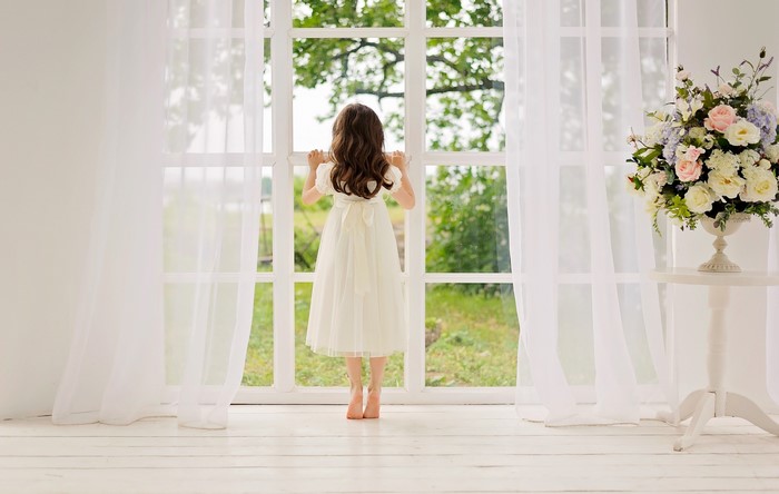 Girl in a white dress looking out a window