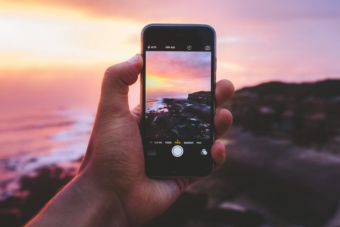 Hand holding iPhone taking picture of sunset over ocean