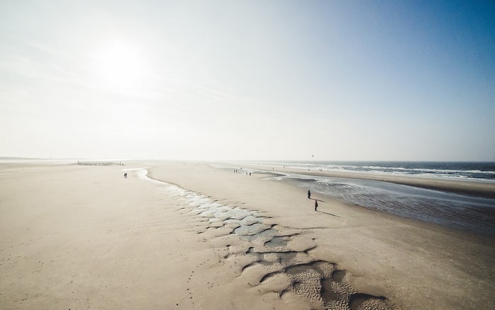 People walking on a wide sandy beach with the sea and sky