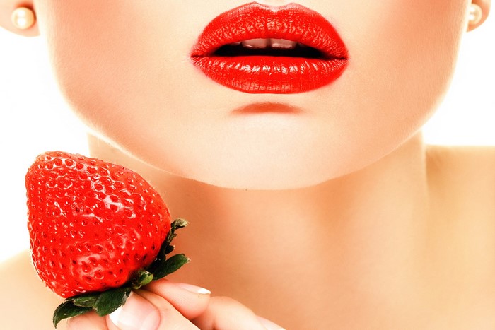 Woman with red lips holding a strawberry