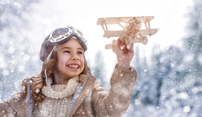 Girl in pilot hat holding toy airplane in winter