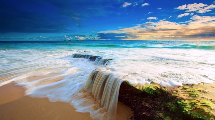 Ocean waves crashing over rocks on a sandy beach