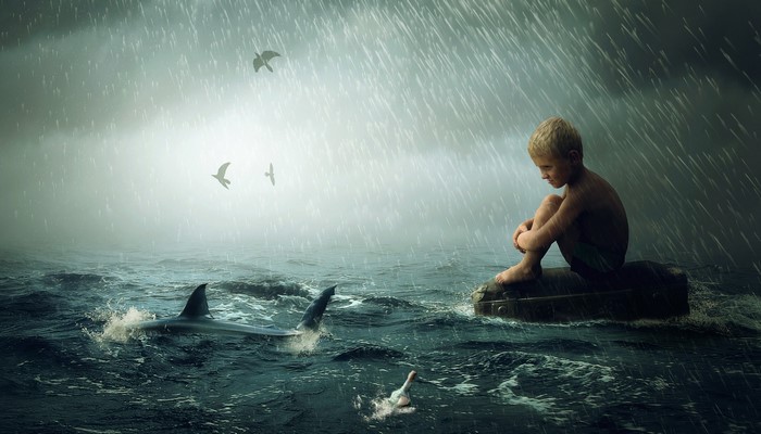 Boy on a suitcase in the sea with sharks and rain