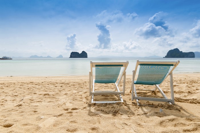 Two beach chairs on a sandy beach with islands in the distance