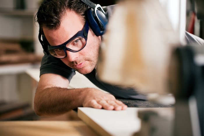 Man wearing safety glasses and headphones using a saw