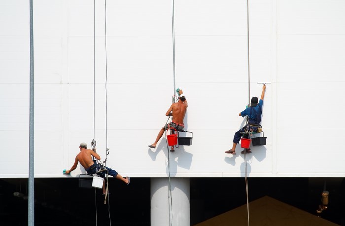 Three window cleaners rappelling down a white building