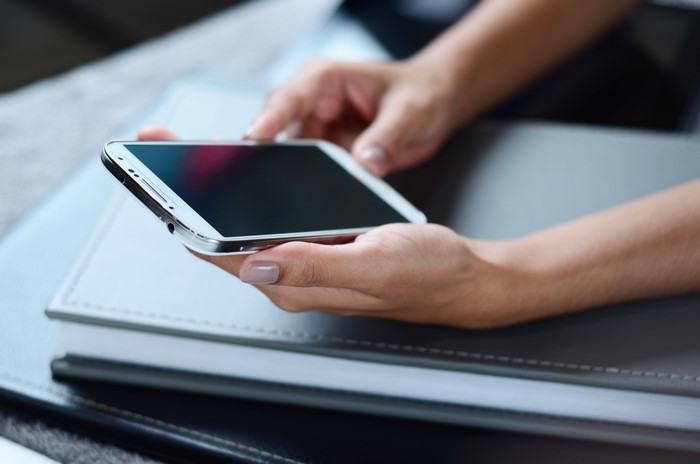 Hands holding a smartphone over notebooks