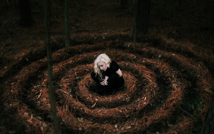 Blonde girl in a spiral of pine needles in a dark forest