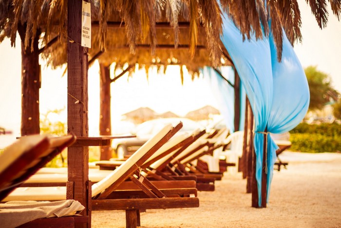 Beach lounge chairs under palm fronds with blue drapes
