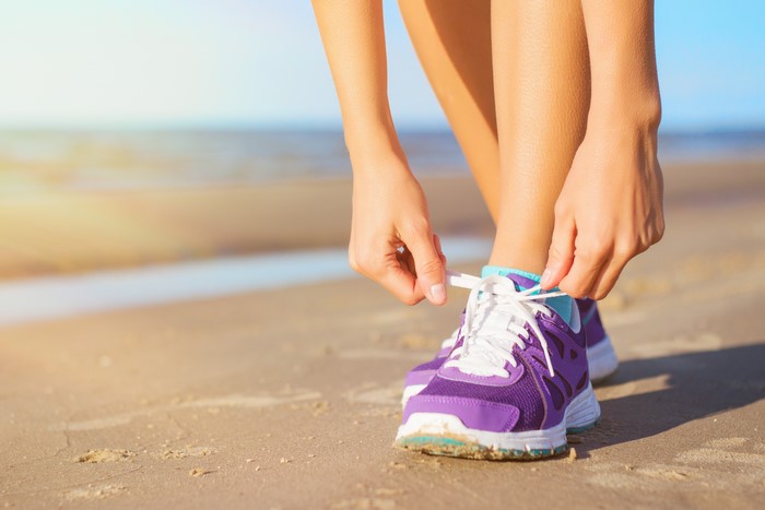 Woman tying purple athletic shoes on beach