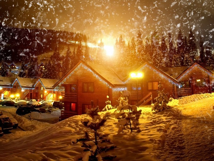 Snowy village with wooden houses decorated with Christmas lights at night