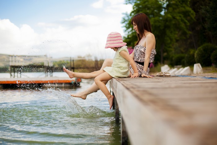 Mother and daughter splashing feet in lake from dock
