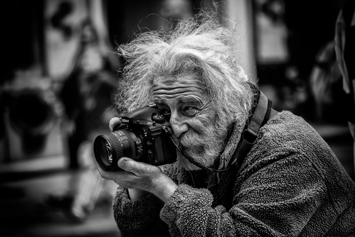 Elderly man with messy hair holding a Nikon camera