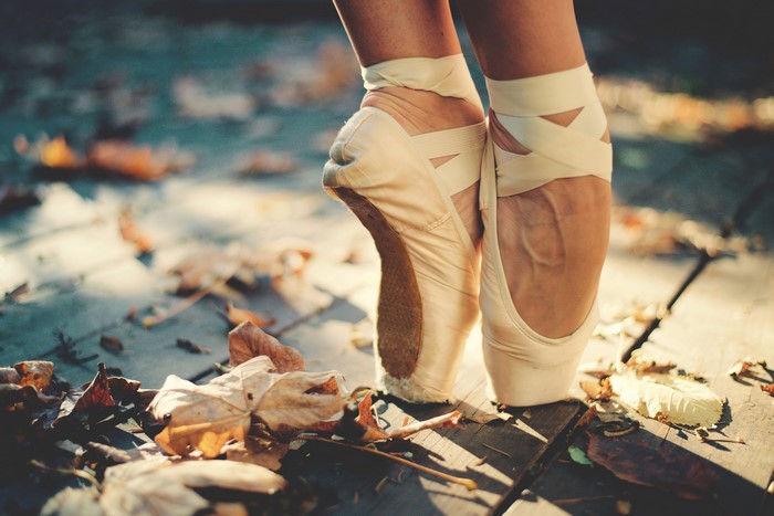 Ballet dancer's feet in pointe shoes on wooden planks with fallen leaves