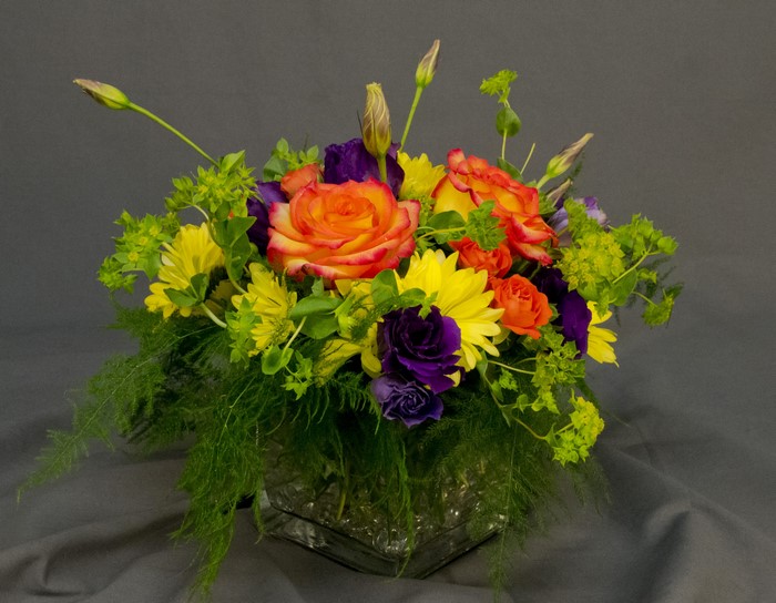 Orange and yellow roses with purple eustoma in a glass vase