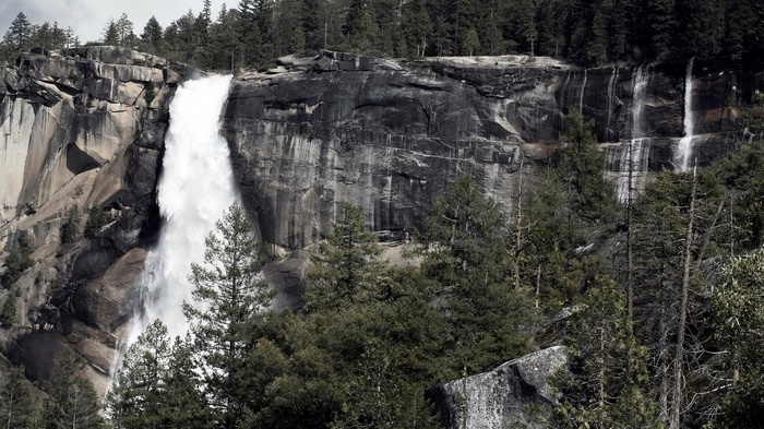 Waterfall cascading down a rocky cliff face with pine trees