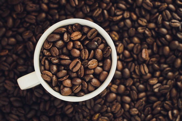 White cup filled with coffee beans on a bed of coffee beans