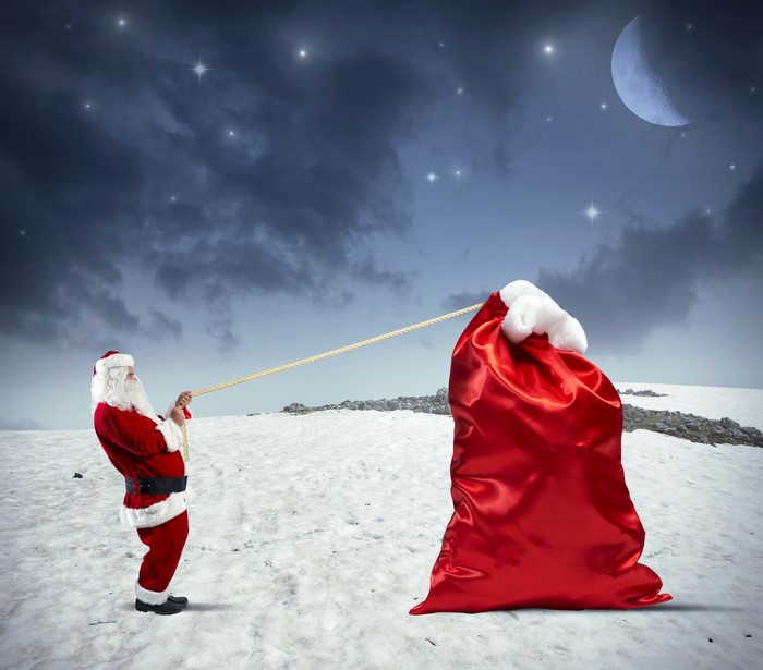 Santa Claus pulling a large gift bag in the snow at night