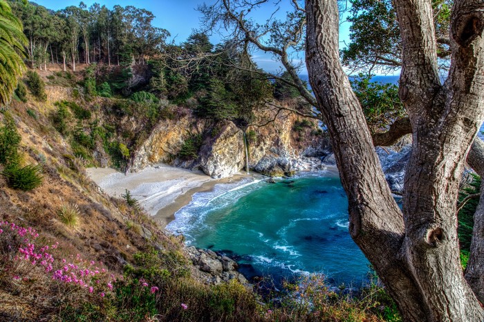 Waterfall cascading onto a beach with trees in the foreground