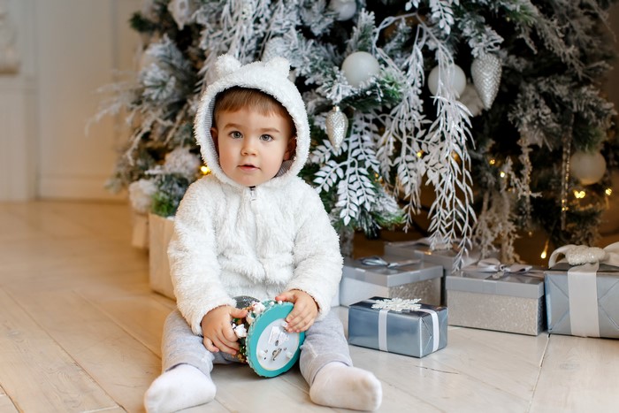 Baby boy in bear costume by Christmas tree with gifts