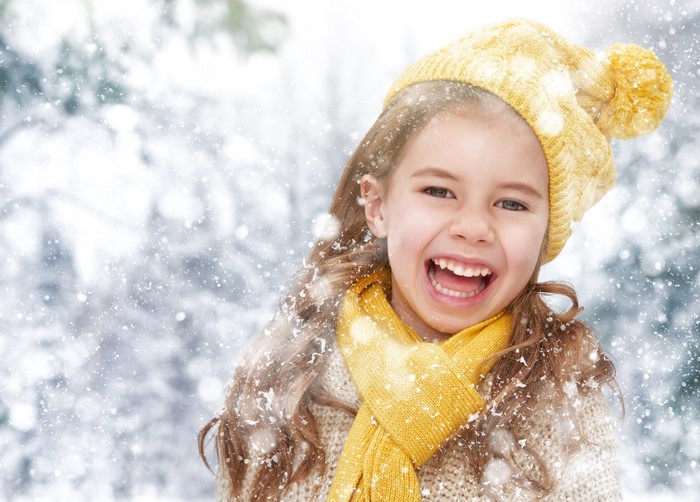 Girl in winter hat and scarf laughing in snow