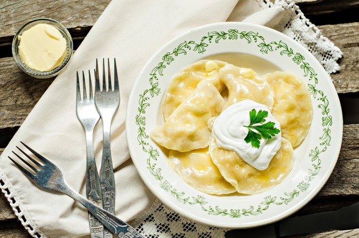 Pierogi with sour cream and parsley on a plate with forks and butter