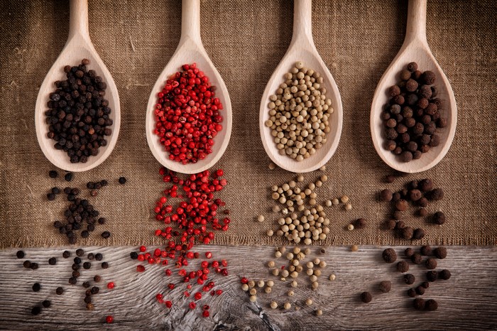 Four wooden spoons filled with different peppercorns